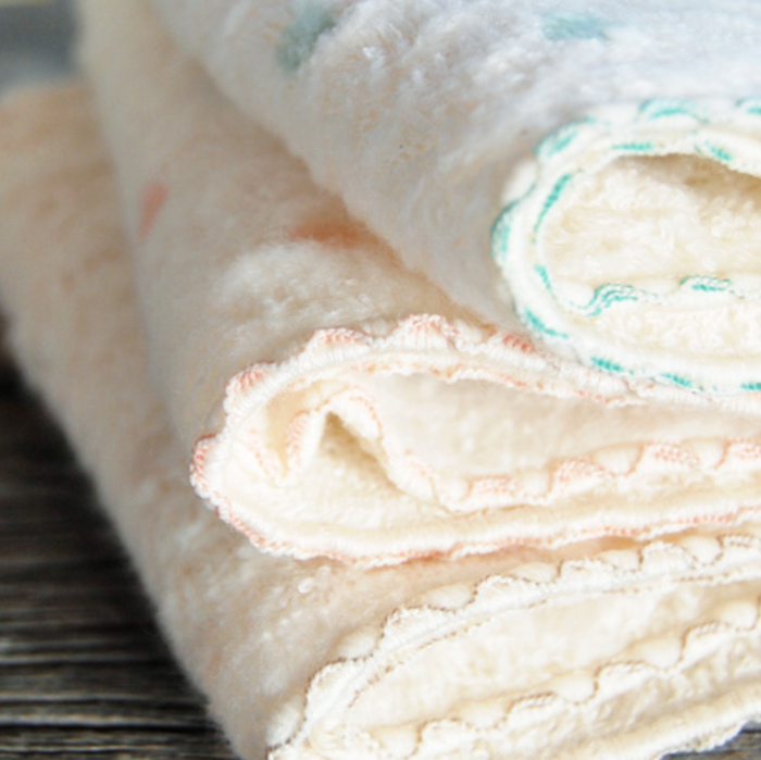 Stack of folded baby washcloths with scallop edge in various colours on a wooden surface.