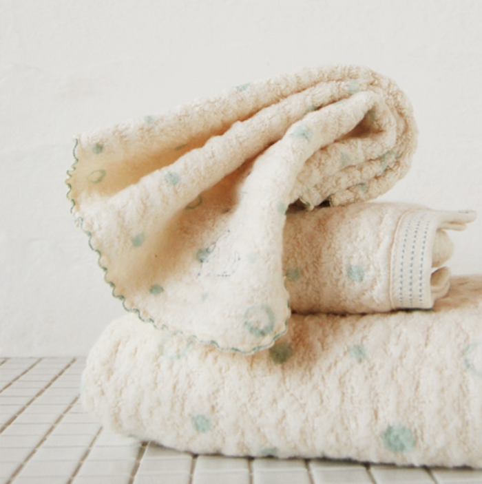Folded cream washcloth and towels with mint blue dot pattern on stack of linens on tiles.