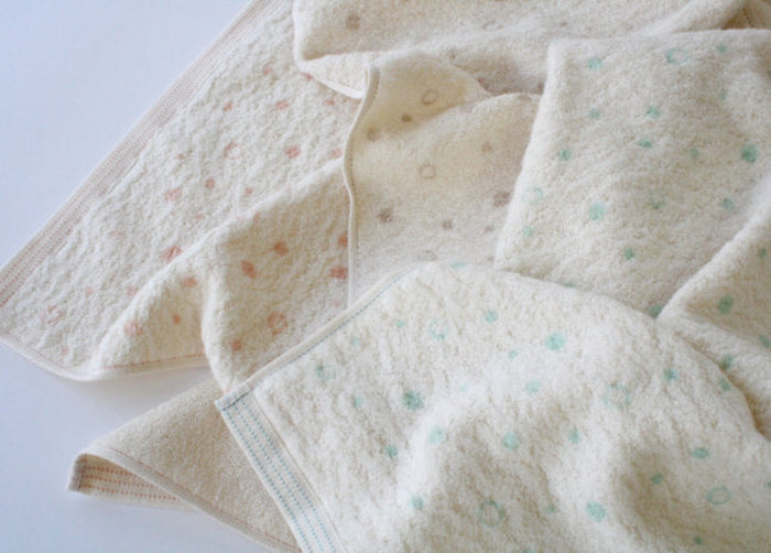 Stack of cream baby hooded towels with polka dots patterns in various colours spread out on a white surface.