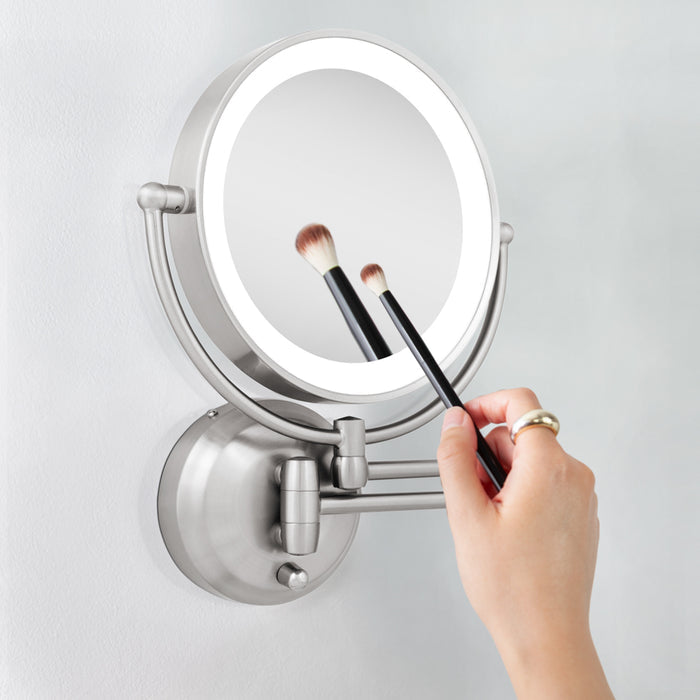 Zadro LEDW410 705004419475 environment photo side view user holding brush to magnified mirror, lighted wall mounted makeup mirror with magnification & extendable arm in front of a real life setting