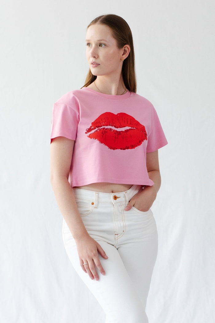 Woman wearing a pink cropped tee with short sleeves and a red lips design on the front.