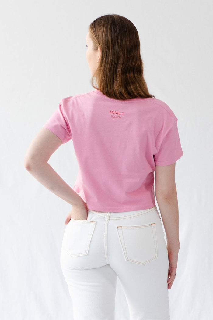 Back of a woman wearing a pink cropped tee with brand name at the top neck.