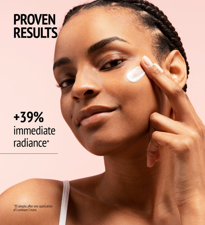 Woman with braided hair applying Luminant Cream | [ comfort zone ] to her cheek, showcasing skincare for immediate radiance and proven results.