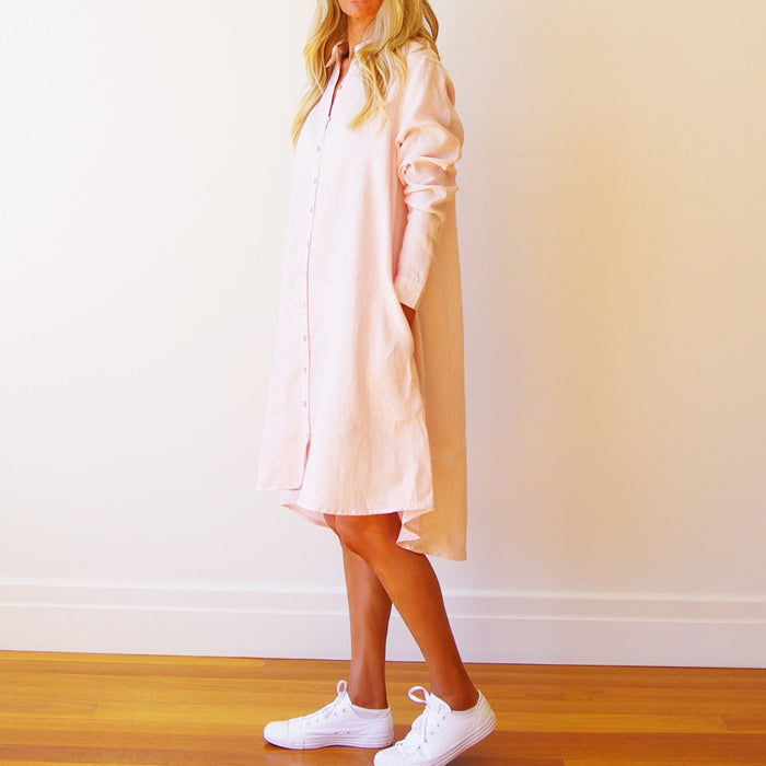 Woman wearing a summer shirt dress in light pink with long sleeves and front buttons.