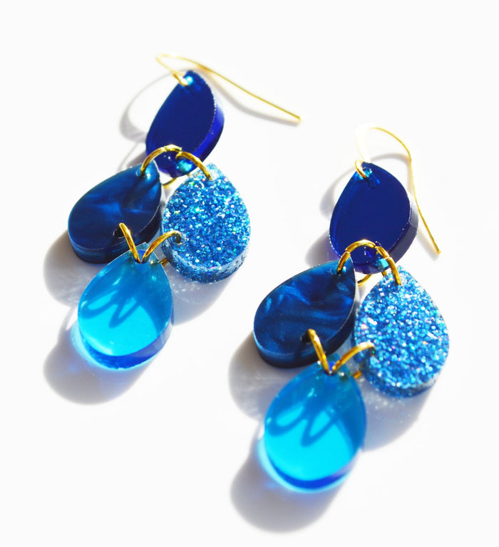 Blue sparkly acrylic dangle earrings in drop shape joined in a chandelier shape on a gold hook.