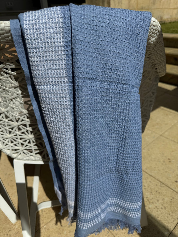 Large light blue waffle weave towel with white striped border hanging over a chair outside - ANNIE.G
