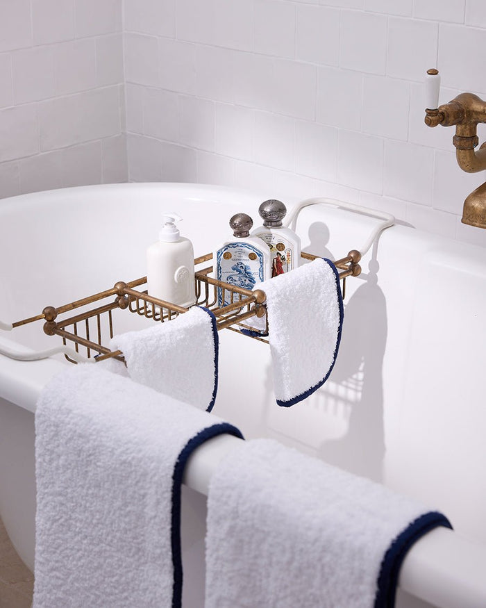 Folded white bath towels with blue bias binding sewn edge hanging on bath tub edge.