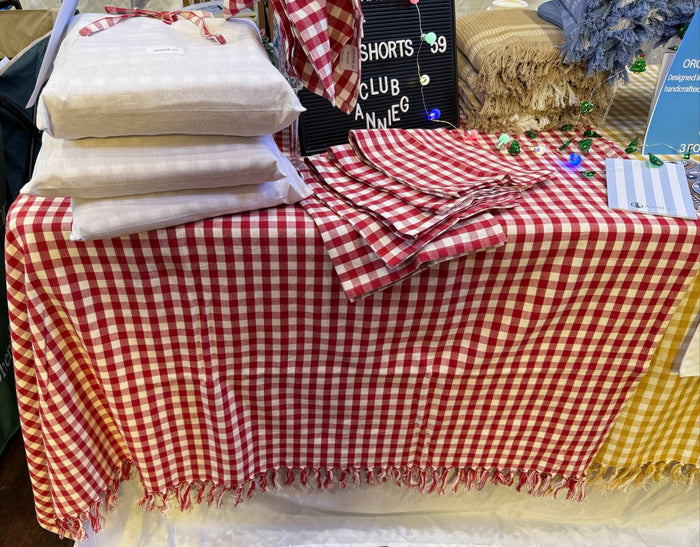Stack of white tablecloth storage bags and red gingham napkins on a red and white checked tablecloth on table - ANNIE.G