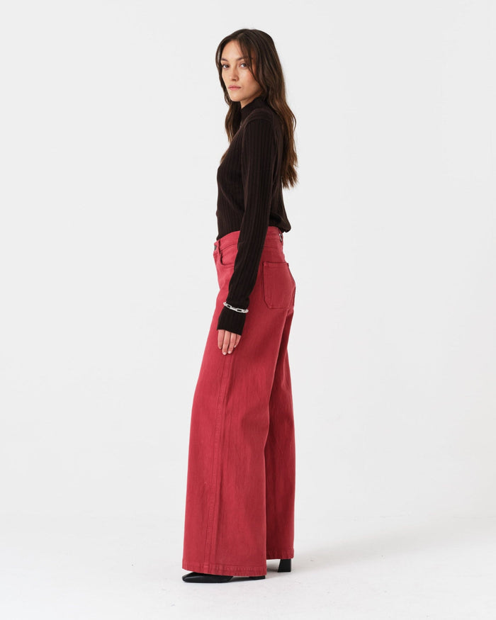 Woman wearing a black top and faded rose pants standing on the side.