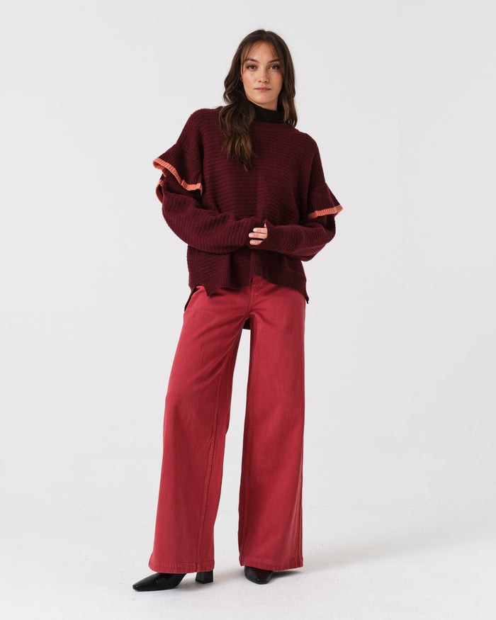 Woman wearing a burgundy sweater and faded rose denim jeans and black boots.