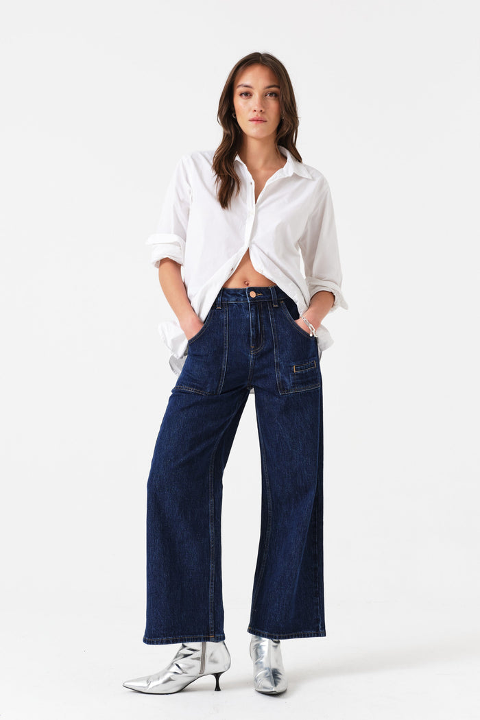 Woman with hands in front pockets of dark blue jeans wearing a white shirt.