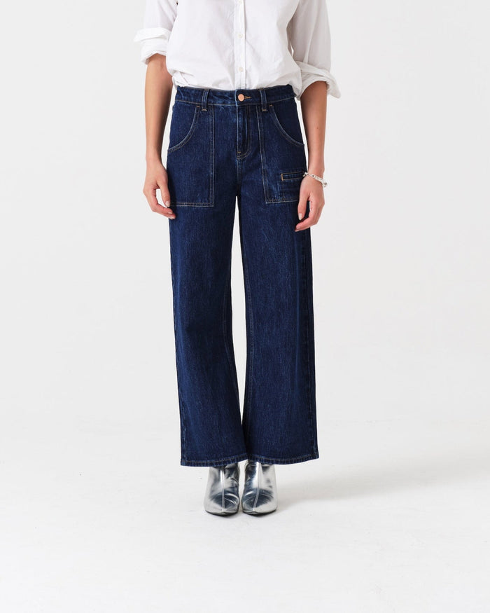 Person wearing cropped blue jeans with retro patch pockets, belt loops, and fly zip with a white shirt.