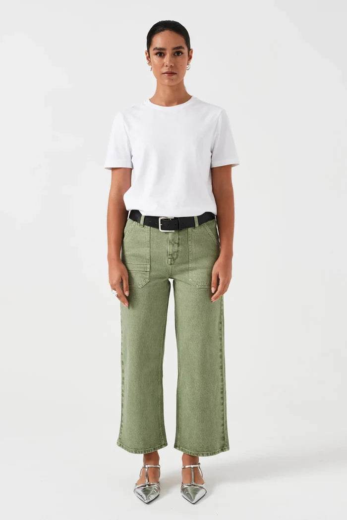 Woman wearing cropped green jeans with pockets and a black belt through loops with a white tee and sandals.