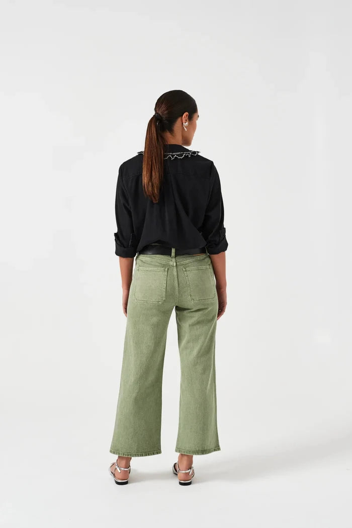 Woman facing backwards wearing green denim jeans with pockets a black shirt and sandals.