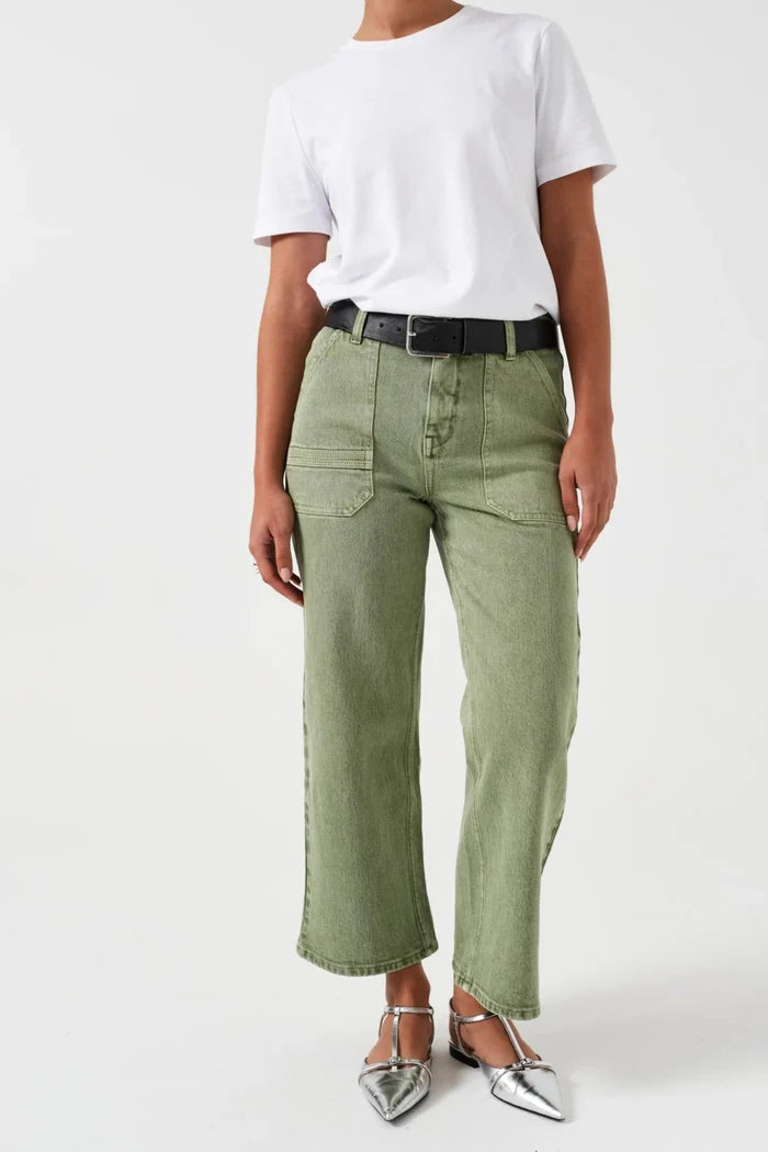 Woman wearing green denim jeans with patch pockets and sandals with a white tee.