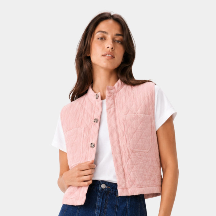 Woman wearing a pink quilted vest over a white shirt and denim.