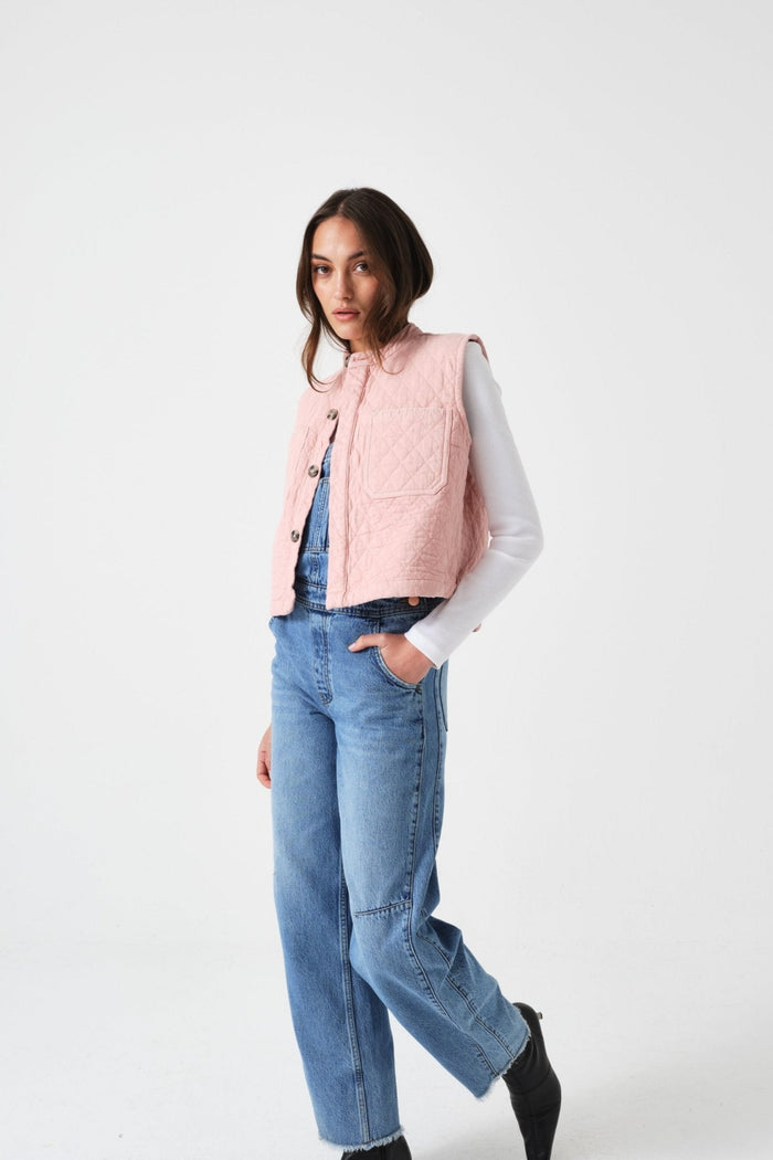 Woman wearing a pink quilted vest with buttons open over a white shirt with blue jeans.
