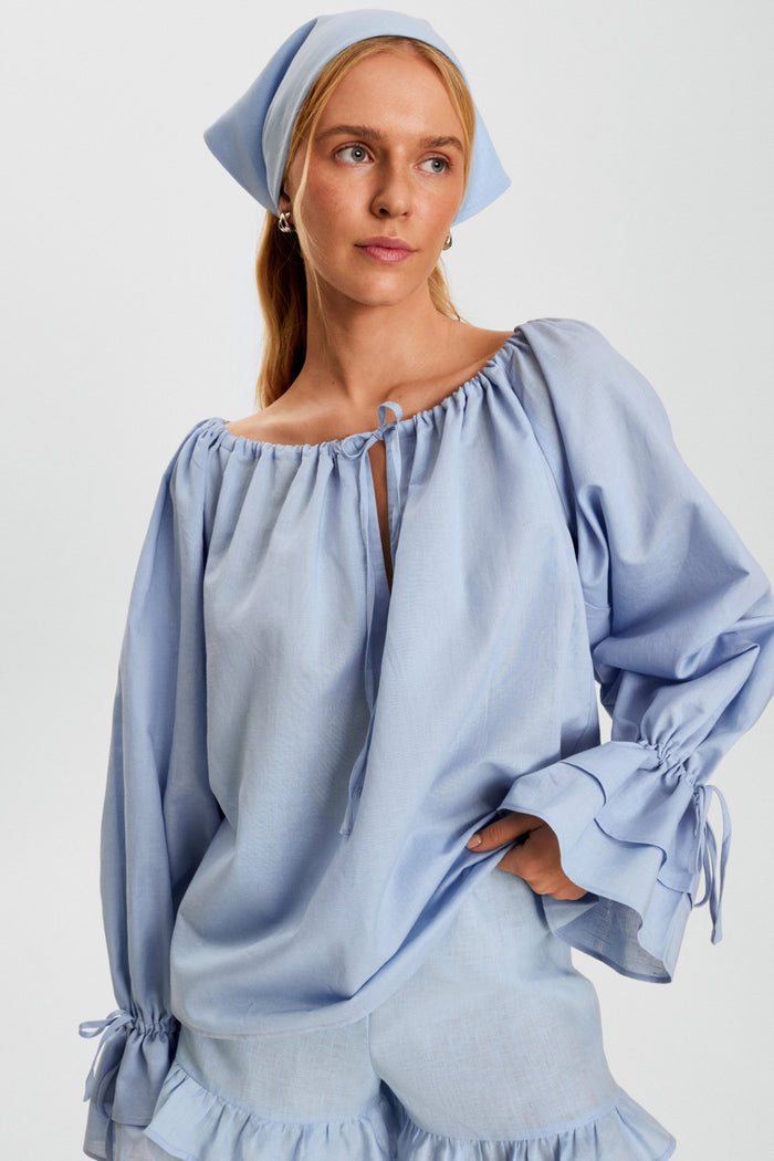 Woman wearing a blue lounge short with frill and a matching blue headscarf and long sleeve top.