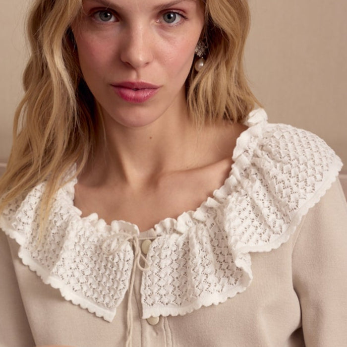 Woman wearing a beige knitted cardigan with lace details and front buttons sitting on a couch.