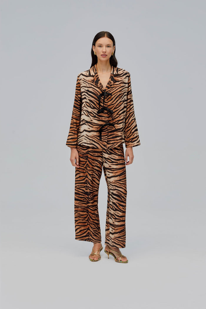 Woman wearing a long sleeve tiger print shirt with collar and ties closure and long pants.