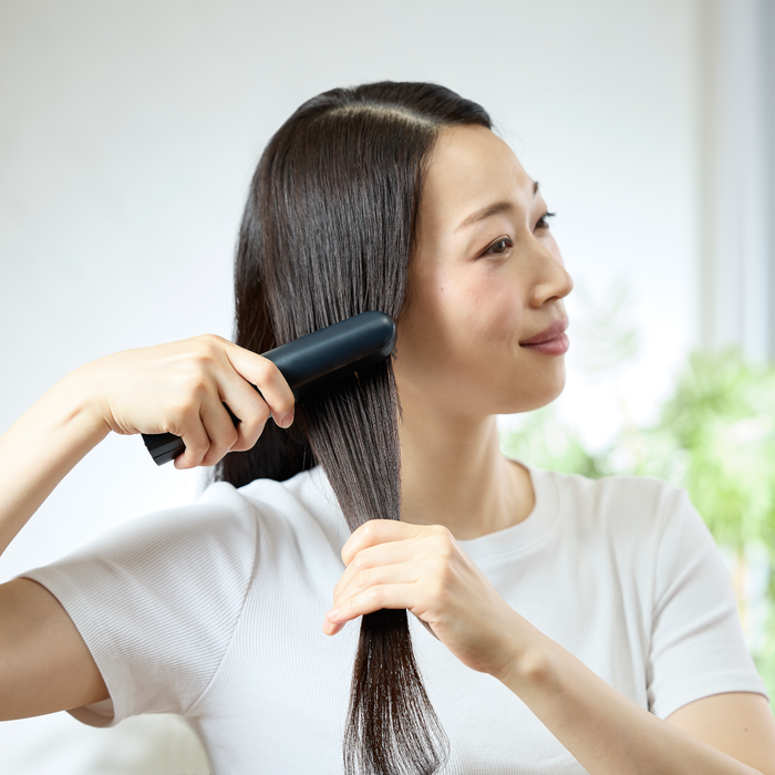 Woman brushing her hair with a black brush against a white background