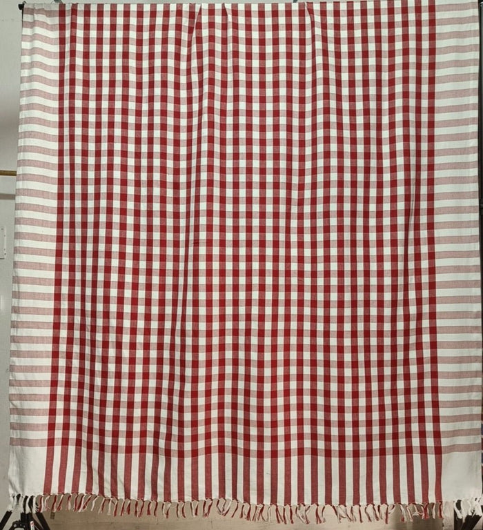 A hanging rectangular tablecloth in red check bordered by red and white stripe and a handknotted fringe.