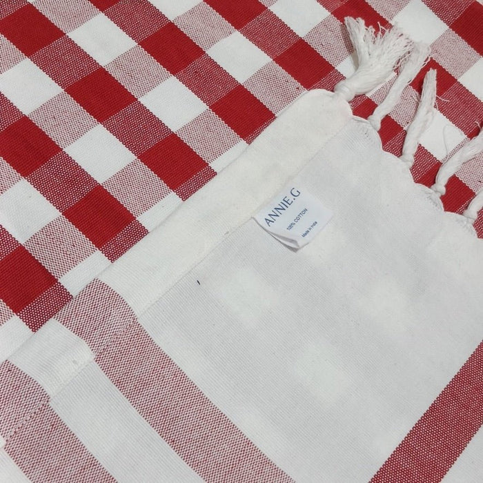 Hem and fringe edge with ANNIEG brand label on red and white checked tablecloth.