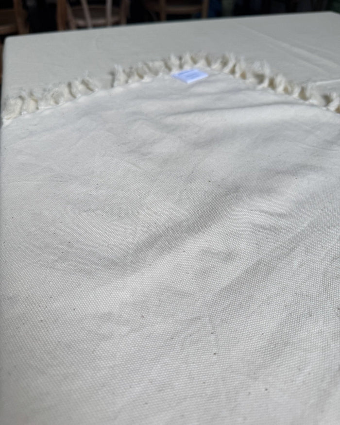 Tablecloth Cotton Square in Natural with a fringe edge folded back showing brand label - ANNIE.G