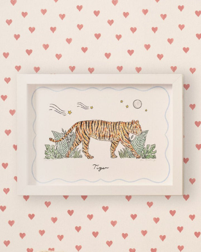 A framed Tiger Print hanging on a nursery wall in a white frame with red heart wallpaper on the wall - ANNIE.G