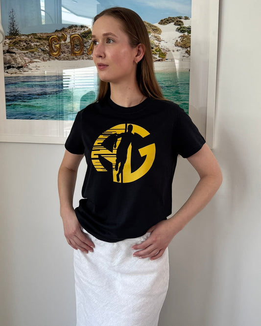 Person wearing a navy t-shirt with a yellow AG logo and running person in front of a scenic painting.